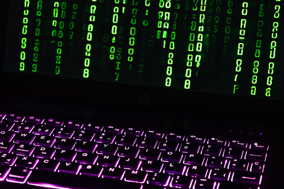 Conceptual cyber scene: green code on a dark laptop over a backlit keyboard — illustrating this week's threat brief.