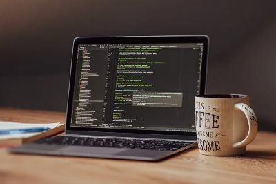 Laptop displaying code editor with coffee mug on desk, perfect for tech themes.