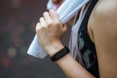 Side view of crop faceless female athlete in black smart watch and sports clothes holding cotton towel after practicing sport outdoors