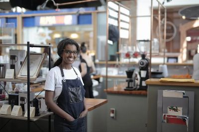 Smiling barista standing in a stylish café, showcasing entrepreneurial spirit.