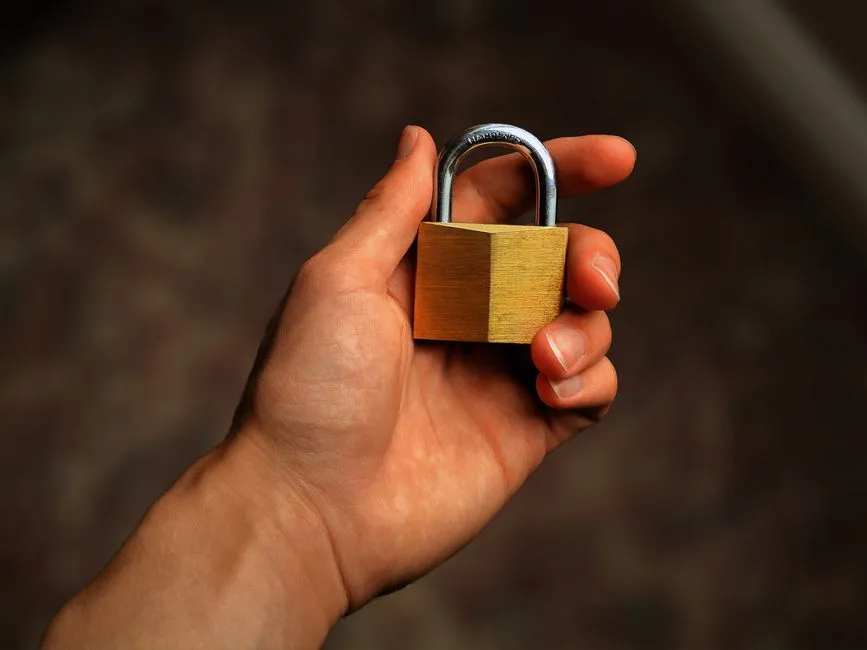 A hand holding a brass padlock, illustrating identity and access security.