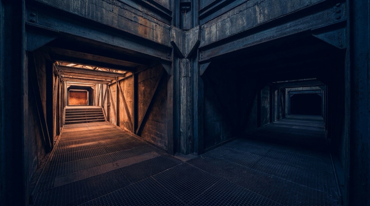One industrial structure whose two corridors diverge, the left rising into light and the right descending into shadow — illustrating one company's two divisions moving in opposite directions.