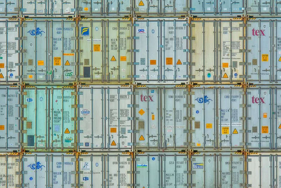A wall of stacked shipping containers seen flat-on, forming a grid of doors in pale green and grey
