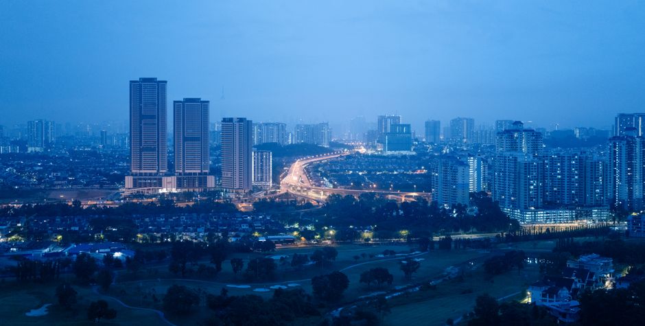 Kuala Lumpur at blue hour from above, dense high-rise housing and lit expressways under a deep navy sky.