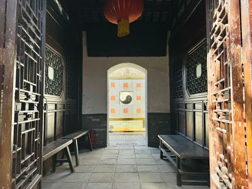 Looking through a traditional Chinese timber doorway to an inner screen bearing a taiji symbol set in a tiled grid