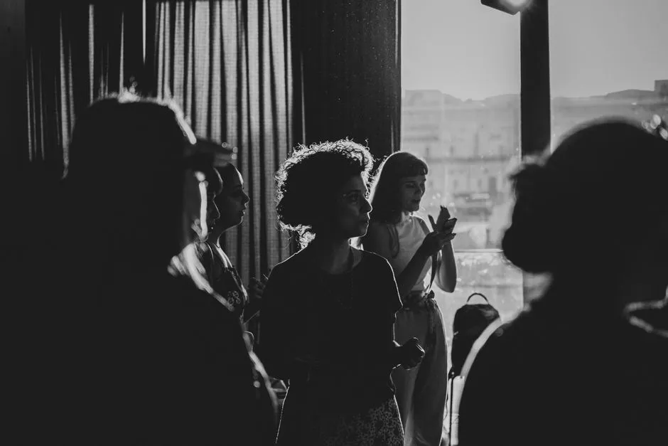 Silhouettes of a diverse group of people gathered near a window in warm backlight