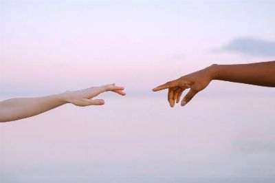 Two diverse hands reaching out across a pastel horizon, symbolizing unity and connection.