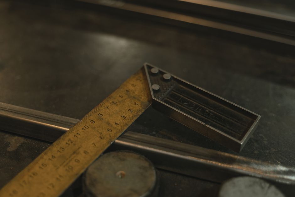 A brass folding rule and a steel try-square lie on a scratched workbench under raking light, the graduations catching the beam.
