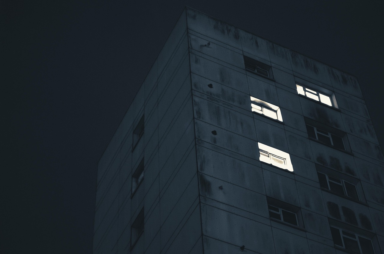 The corner of a dark residential block at night with only three windows lit.