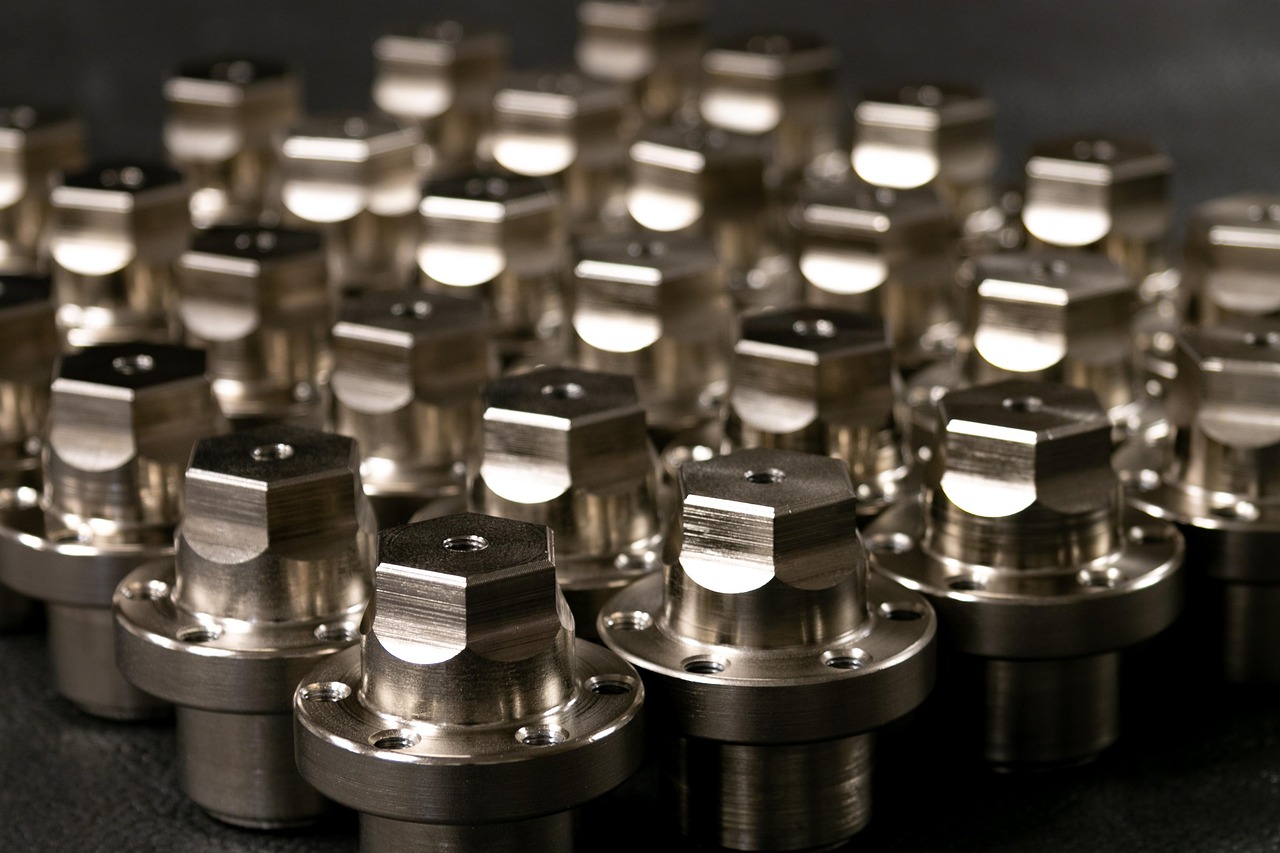 Dozens of identical freshly machined brass flanged parts stand in rows on a dark bench, warm light picking out the cut faces.