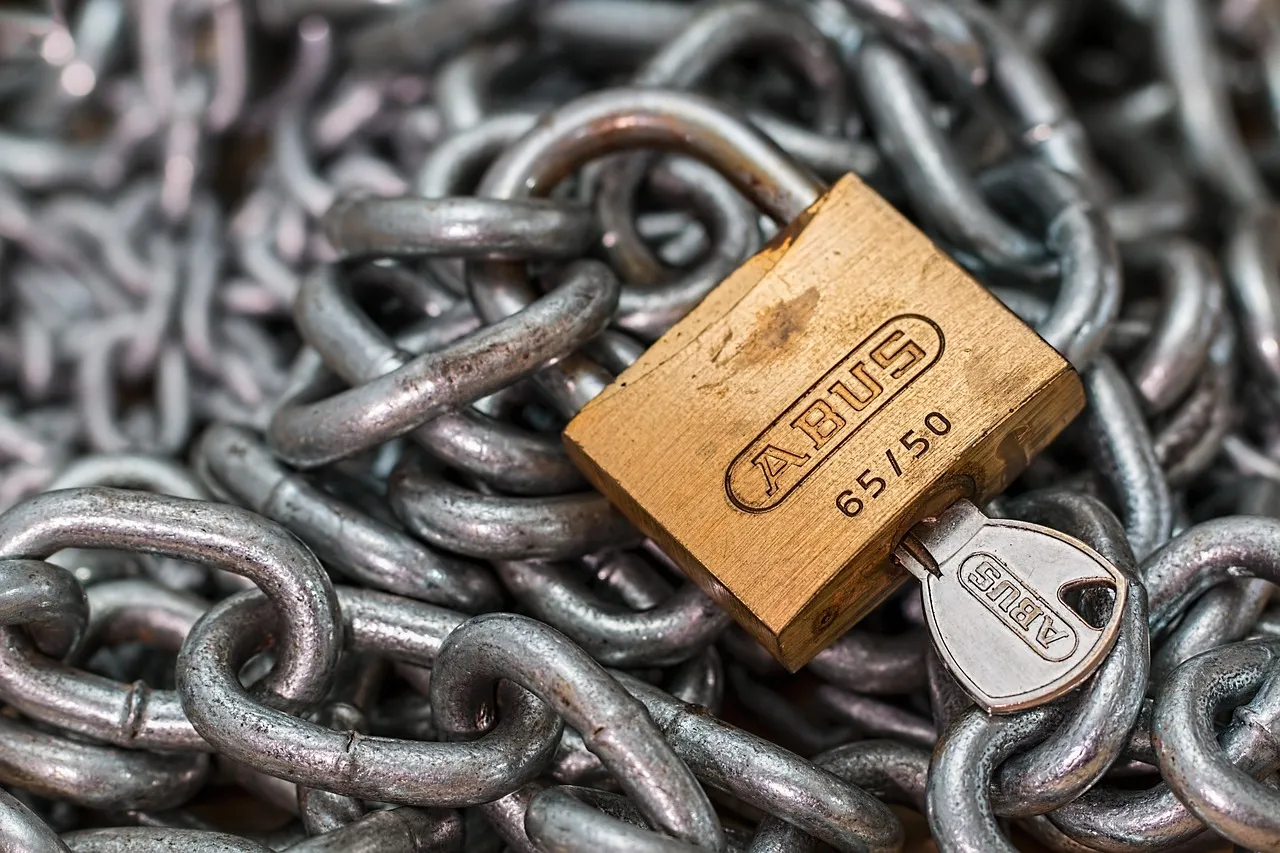 A brass padlock and key resting on steel chains
