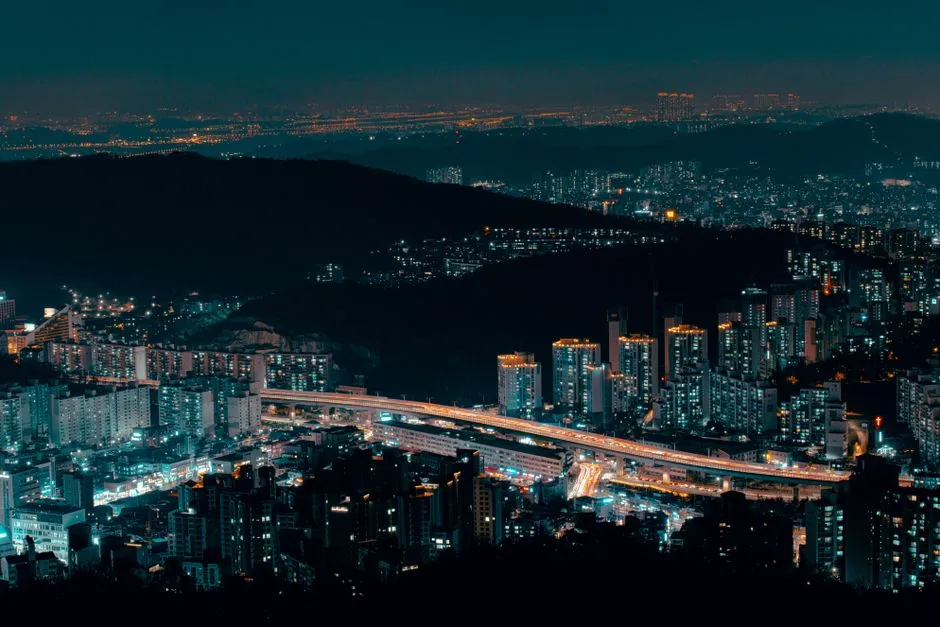 A South Korean city at night with apartment towers and an elevated expressway, illustrating a report on record shareholder returns from Samsung and SK Hynix.