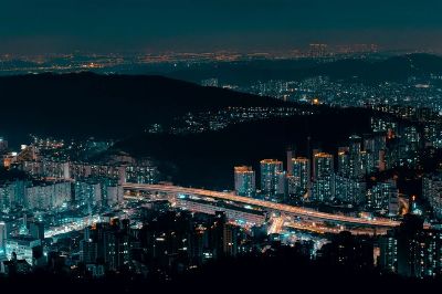 Aerial view of a vibrant cityscape with illuminated buildings and a winding highway at night.