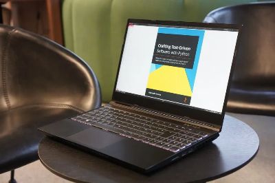 A close-up of a laptop on a table, displaying a book on test-driven software with Python, set in a comfortable environment.