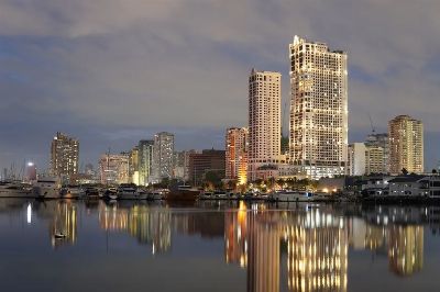Stunning twilight view of Manila's skyline reflecting on a calm body of water, featuring tall buildings and a serene atmosphere.