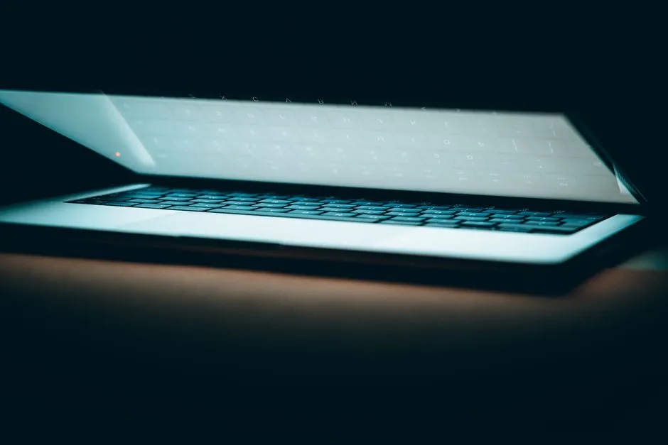 A laptop lid half open, its screen glowing in a dark room