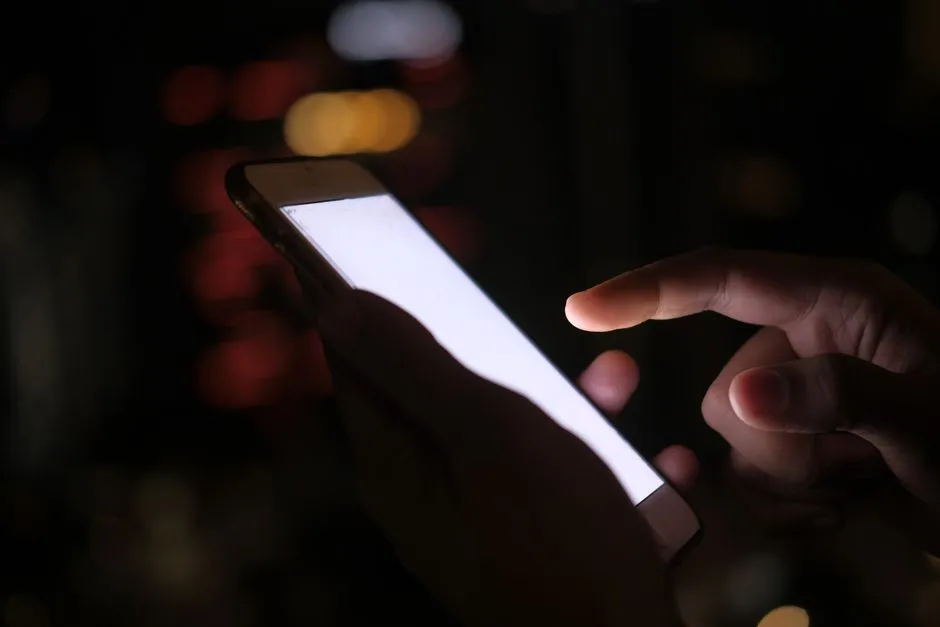 Two hands holding a phone with a blank, bright screen in the dark, city lights blurred behind it — illustrative of the late-night engagement the New Mexico ruling is about.