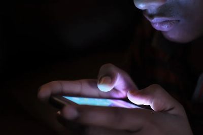 Close-up of a person holding and using an illuminated smartphone in a dark setting.