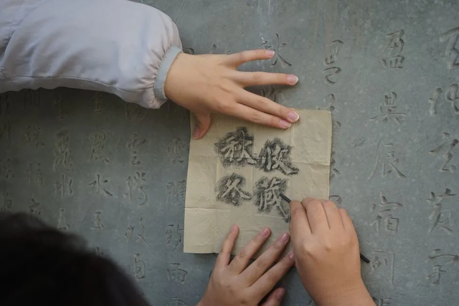 Hands taking a paper rubbing of Chinese characters carved into a stone tablet