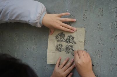 Close-up of hands using charcoal to trace Chinese characters on a stone wall, highlighting calligraphy art.