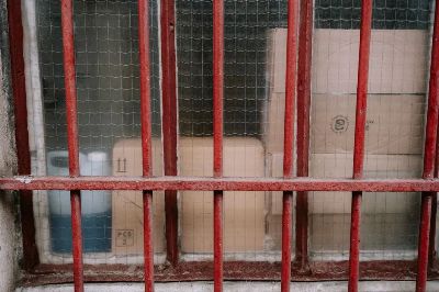 Cardboard boxes behind red metal grid window in warehouse.