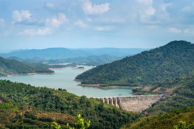 Aerial view of a serene mountain reservoir with a dam surrounded by lush green hills.