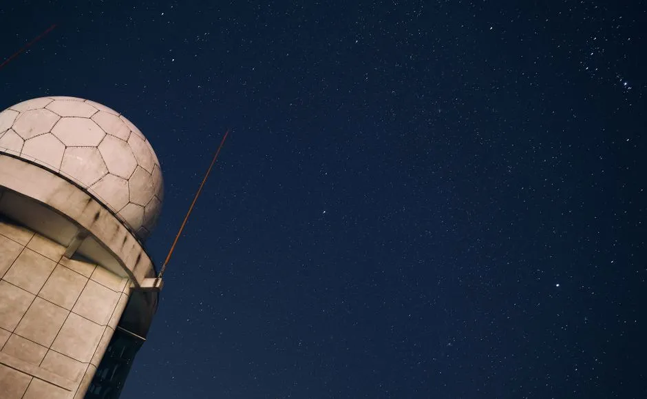 A geodesic radome silhouetted against a dense field of stars