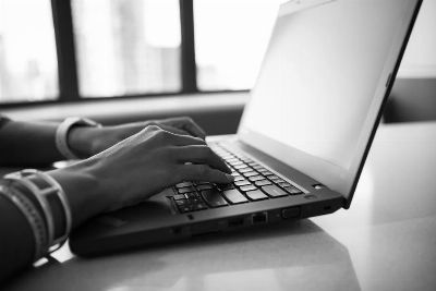 Close-up black and white photo showing hands typing on a laptop, emphasizing modern technology.