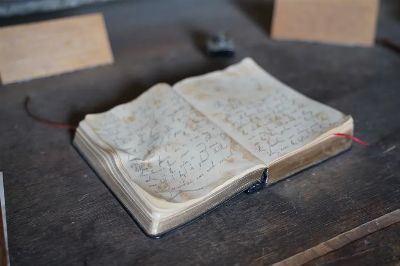 A close-up of an antique open book with handwritten pages on a rustic wooden table.