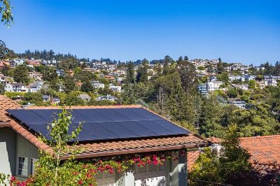 Solar panels on a suburban home, surrounded by lush greenery and a sunny blue sky.
