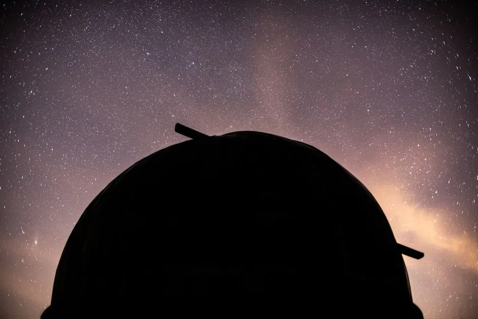 The dome of an astronomical observatory silhouetted against a dense star field and the band of the Milky Way