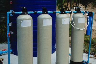 Four beige tanks in an outdoor water treatment setup with blue piping.