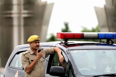 Police officer standing beside patrol car holding a radio microphone outdoors.
