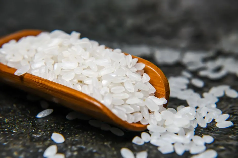 A close-up image showcasing uncooked rice grains in a wooden scoop on a textured dark surface.