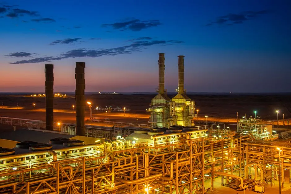 A refinery lit up at dusk, its pipework and stacks silhouetted against a blue sky, illustrating a report on autonomous industrial inspection robots.