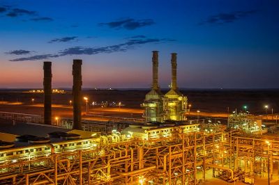 Aerial view of an illuminated factory with chimneys at sunset, showcasing industrial architecture.