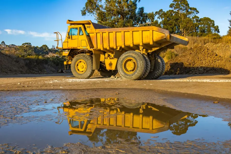A yellow mining haul truck at a quarry, reflected in a puddle of water