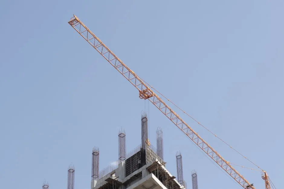 A tower crane above a high-rise under construction, illustrating a report on SK hynix's two new memory fabs and their build schedule.