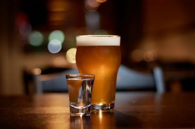 A close-up of a beer glass and vodka shot on a pub table with bokeh lighting.