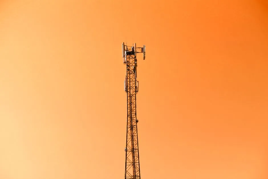 A telecommunications mast carrying panel antennas, silhouetted against an orange sky
