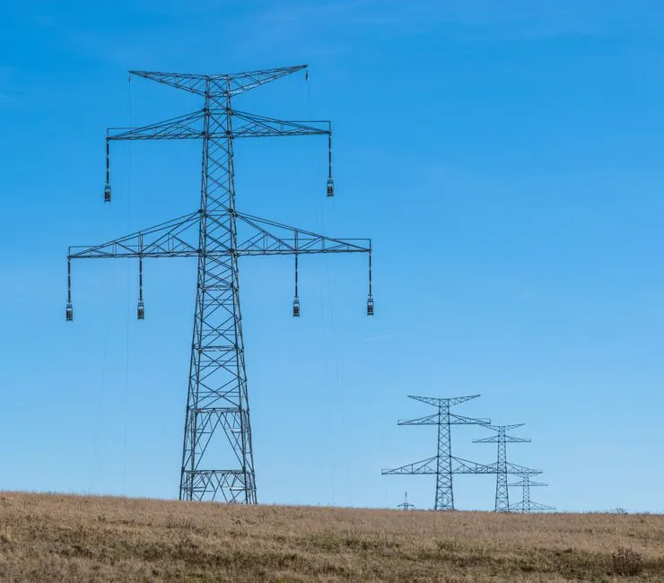 High-voltage transmission towers receding across open ground, illustrating a report on a proposed Philippine AI hub projected to need three gigawatts.