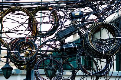Intricate network of tangled power and communication cables outdoors.