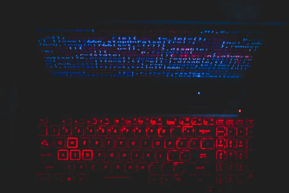 Lines of source code glowing on a dark laptop screen above a red backlit keyboard