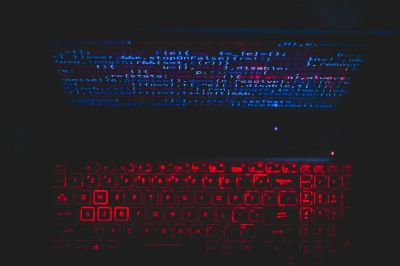 Dark-themed laptop setup with a red glowing keyboard and code on screen, ideal for tech enthusiasts.