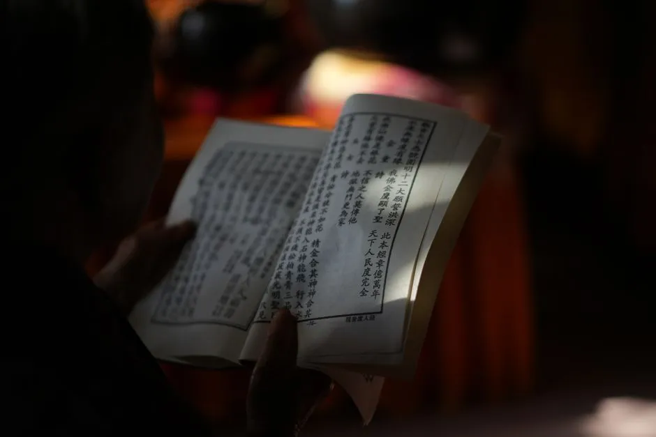 A person reading a printed Chinese book in low light