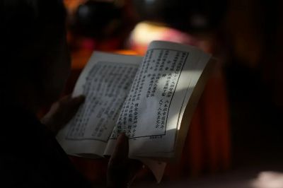 Close-up of hands holding a Chinese book, illuminated softly amidst shadows, emphasizing reading focus.
