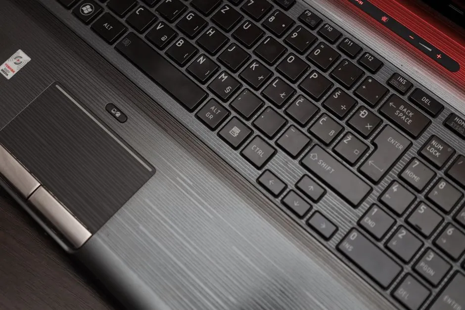 A close-up of a laptop keyboard and trackpad with a small fingerprint reader beside it