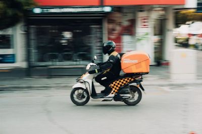 A delivery rider on a motor scooter speeds through city streets capturing urban transportation dynamics.