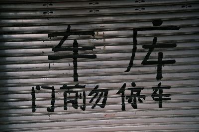 Graffiti in bold Chinese characters on a closed metal shutter in an urban area.