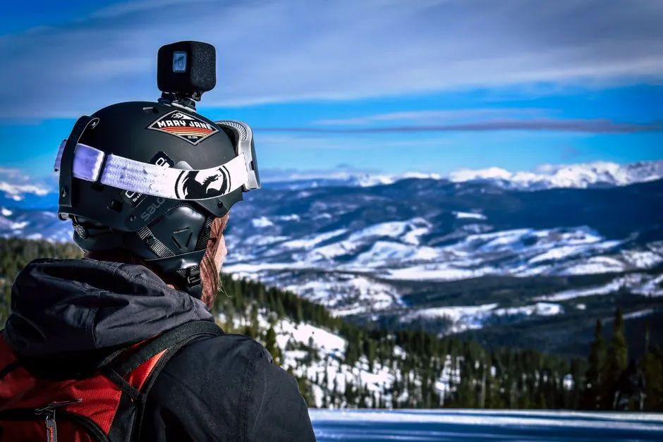 A skier seen from behind with a small action camera mounted on their helmet, looking out over snow-covered mountains
